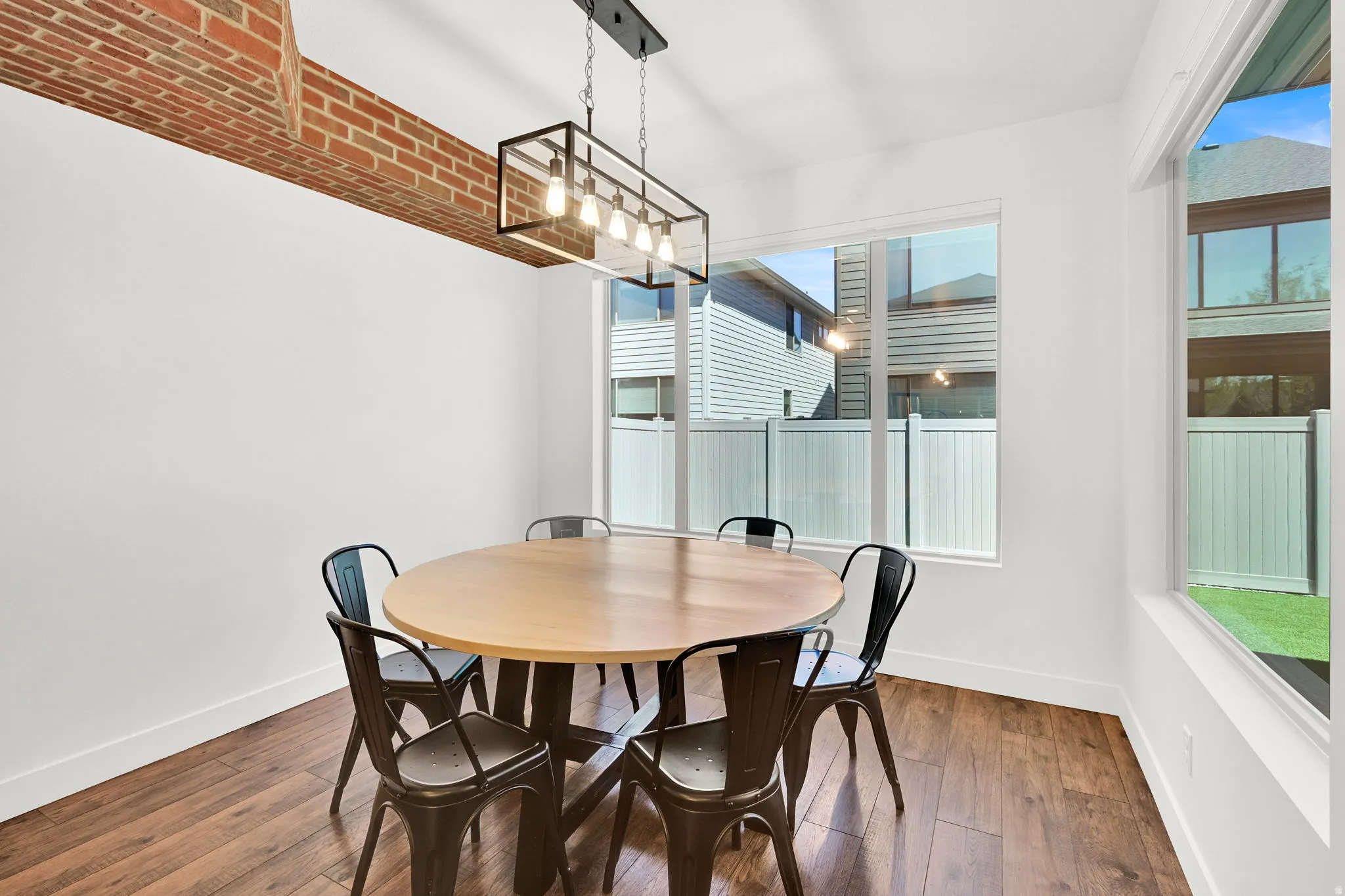 Dining area featuring a linear chandelier, exposed brick architectural detail, and wood-finish flooring
