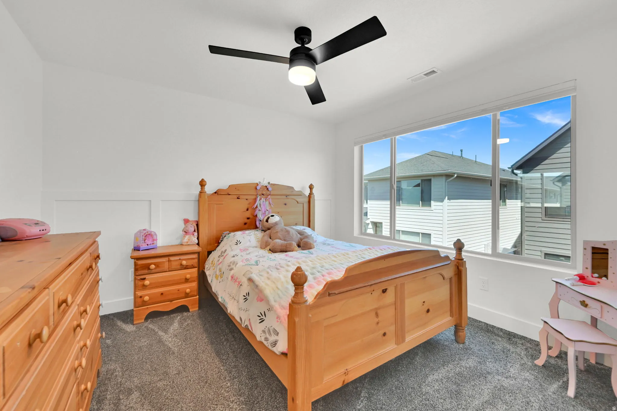 Bright interior space featuring a large picture window, a modern black ceiling fan with integrated lighting, and white board and batten wall detailing