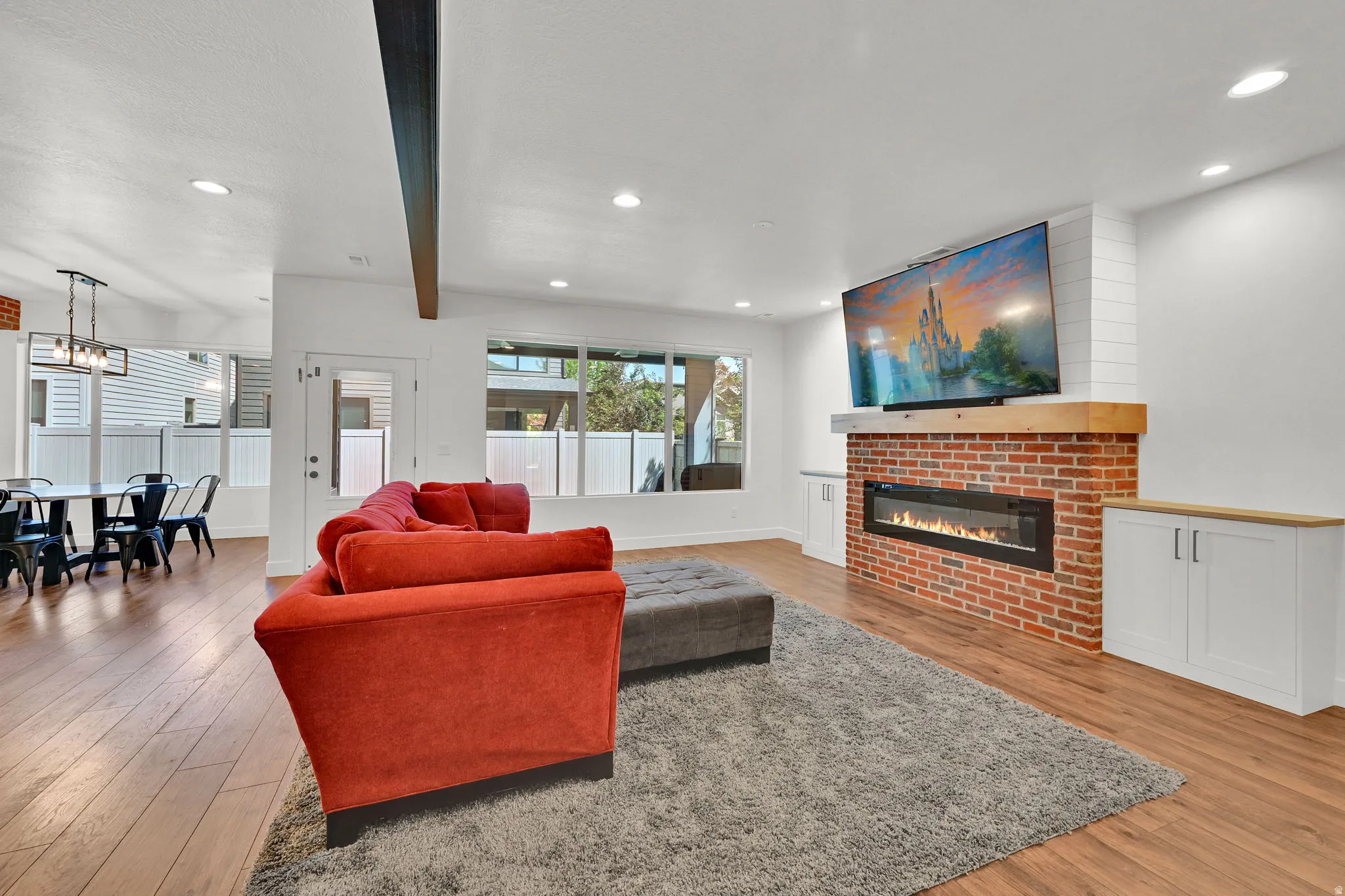 Open-concept living area featuring wood-finish flooring, a contemporary linear fireplace with a brick surround and wood mantel, recessed ceiling lighting, and built-in white cabinetry with wood countertops