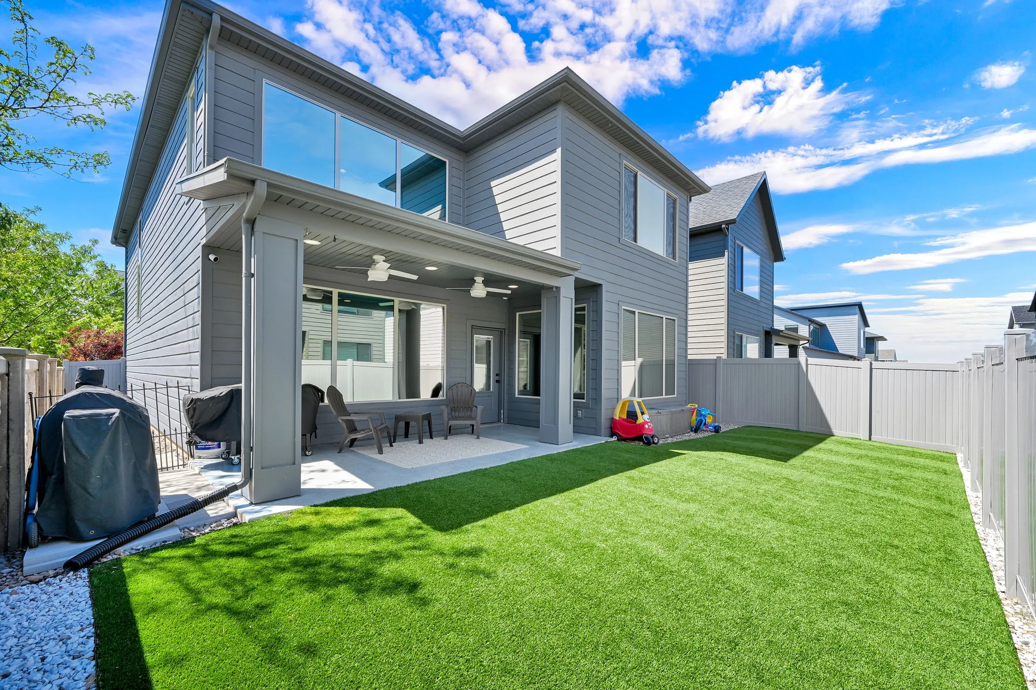 Expansive backyard featuring a covered patio, artificial turf, and privacy fencing. *Notice the tinted windows