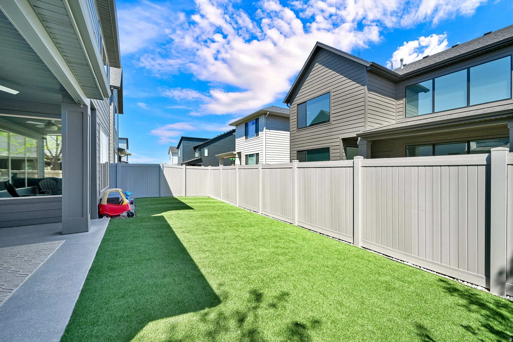 Spacious backyard featuring artificial turf, a light-toned privacy fence, and an extended concrete patio