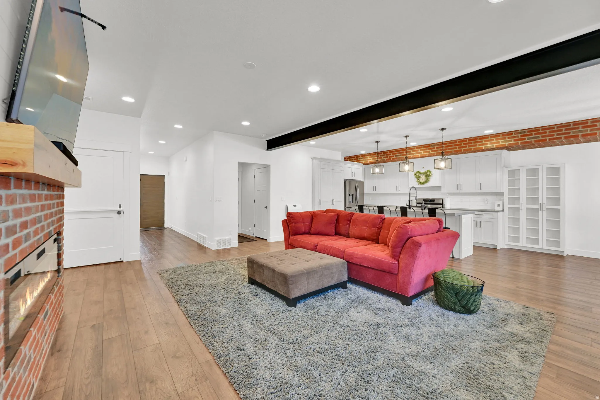 Open-concept living space featuring wood-finish flooring, recessed lighting, and a modern fireplace with a brick surround and wood mantle