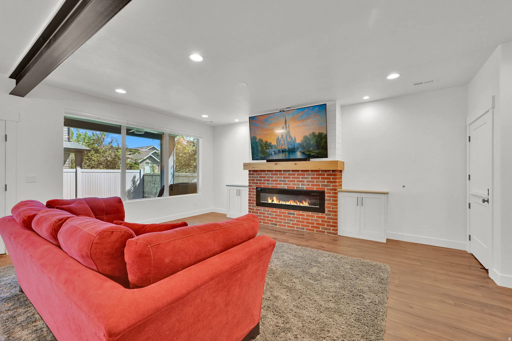 Spacious living area featuring a red brick fireplace with a wood mantel, an integrated linear electric fireplace, and built-in white cabinetry
