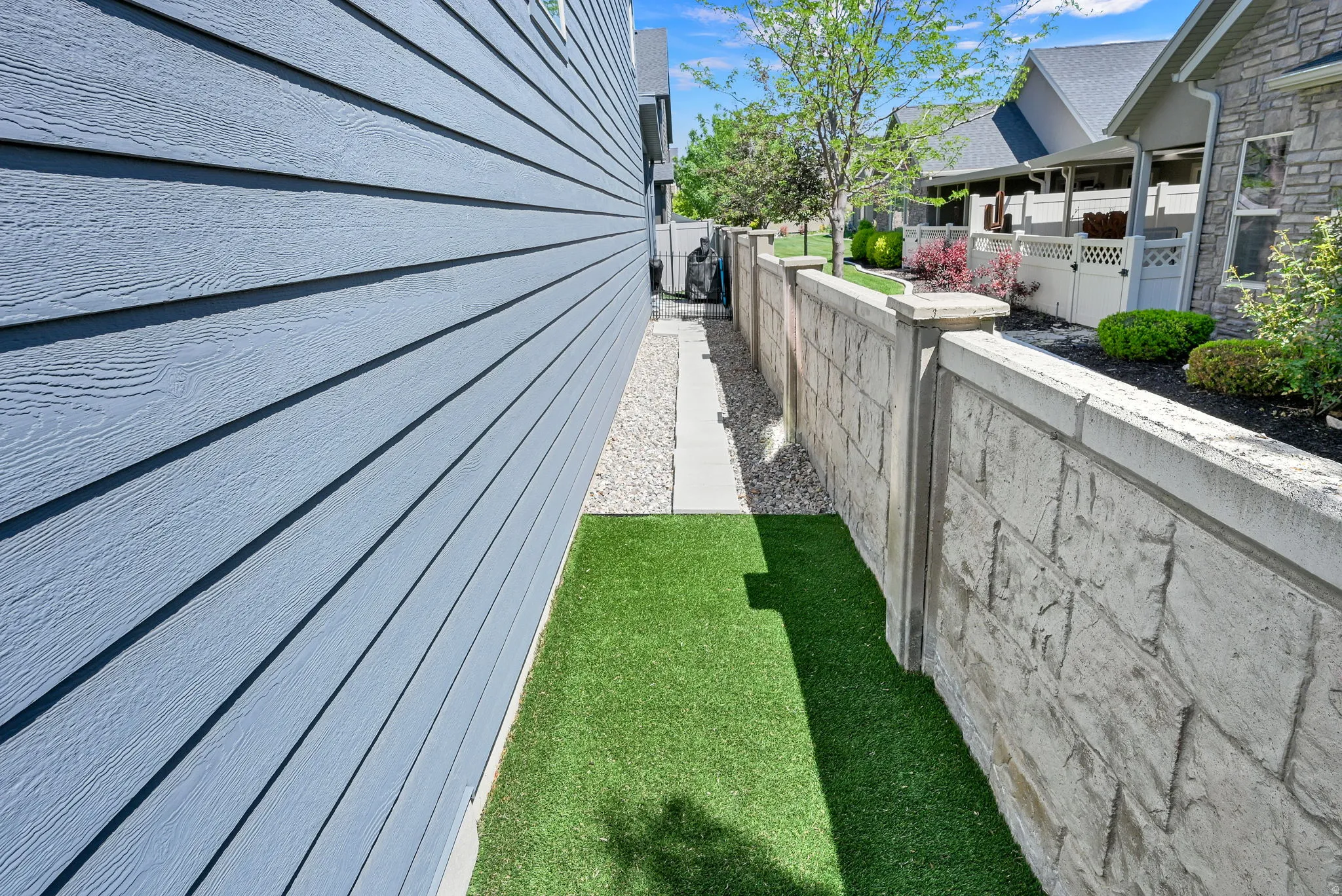 Stone-textured privacy wall bordering a low-maintenance artificial turf strip and gravel pathway