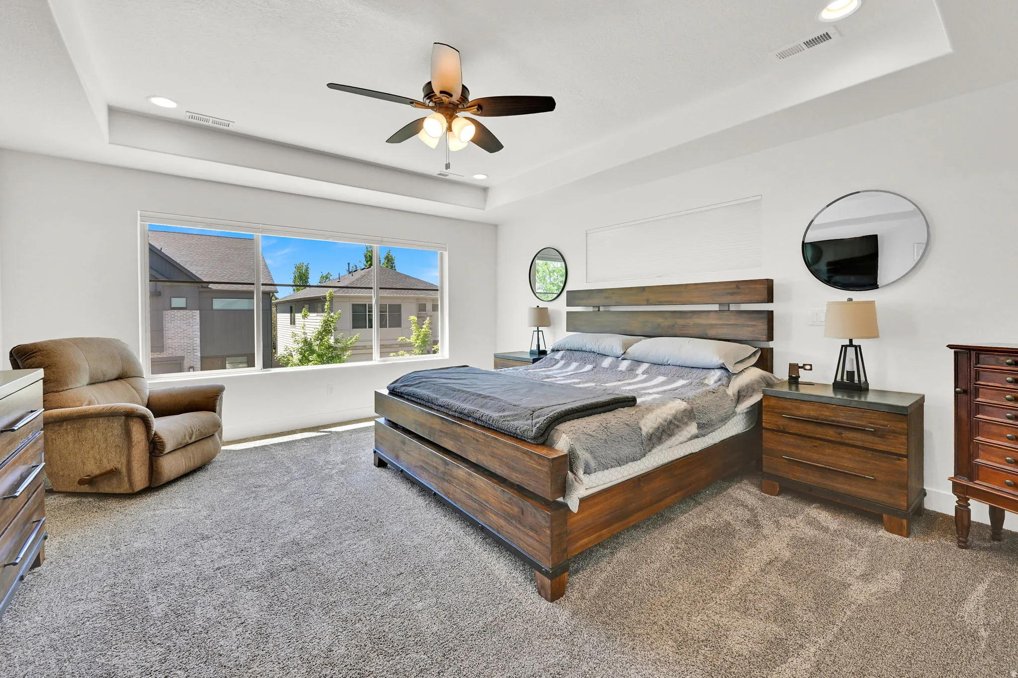 Spacious bedroom featuring a tray ceiling with recessed lighting, a ceiling fan with integrated light fixture, and a large window providing ample natural light
