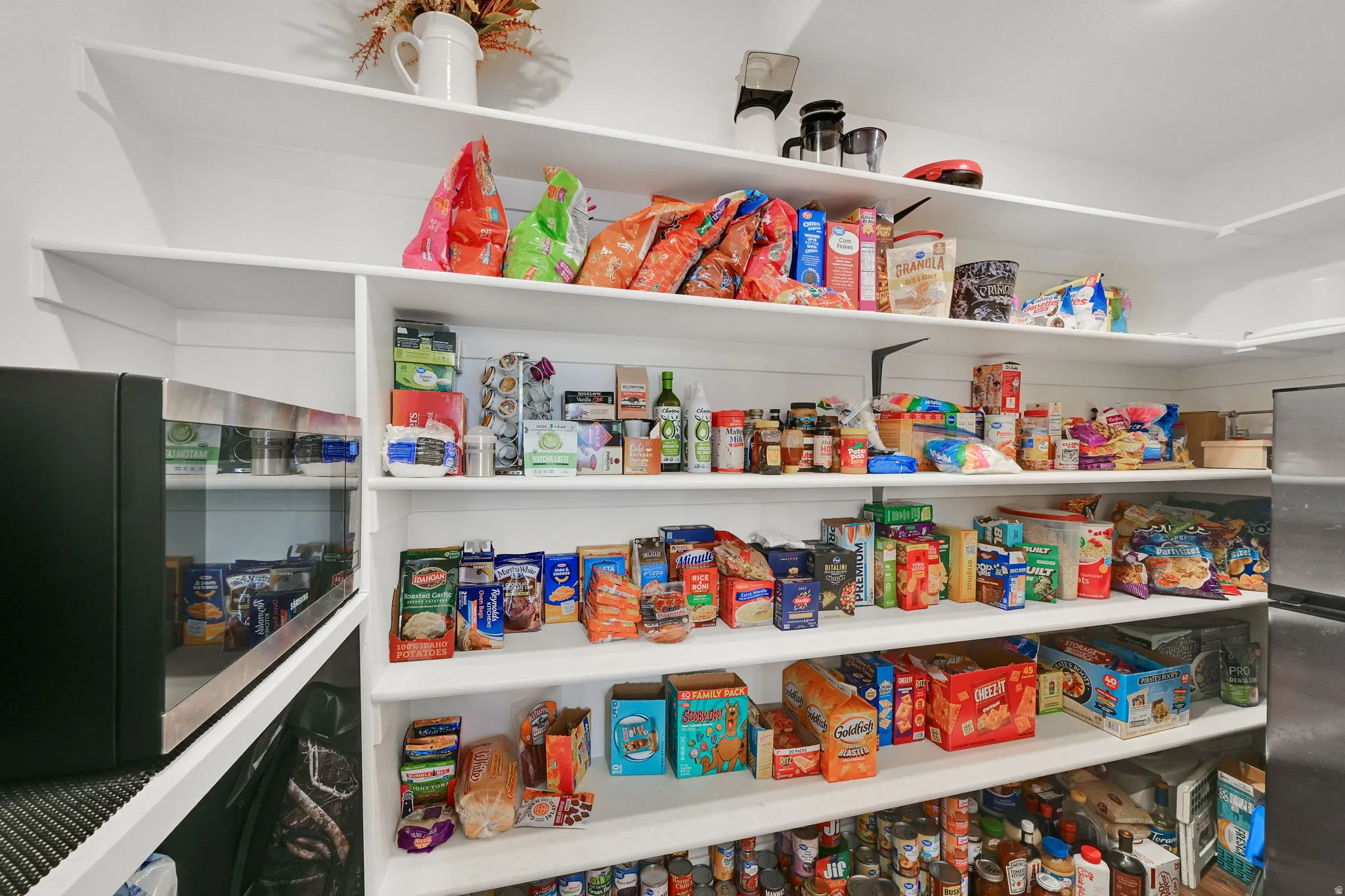 Spacious pantry featuring extensive shelving, a built-in microwave, and a stainless steel refrigerator