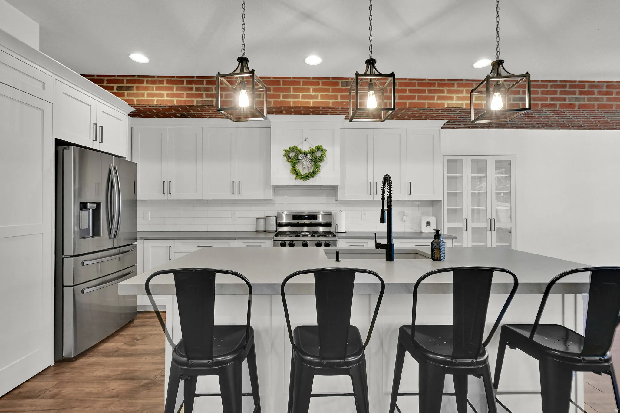 Kitchen featuring a large central island with seating, white shaker-style cabinetry, stainless steel appliances, brick accent wall, and wood-finish flooring