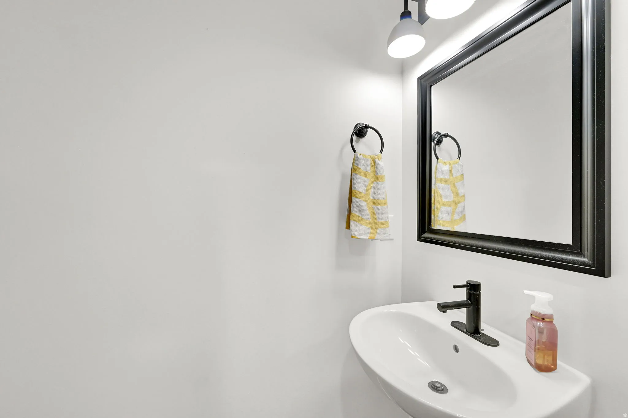 White wall-mounted sink with a matte black faucet, framed mirror, and overhead lighting fixture