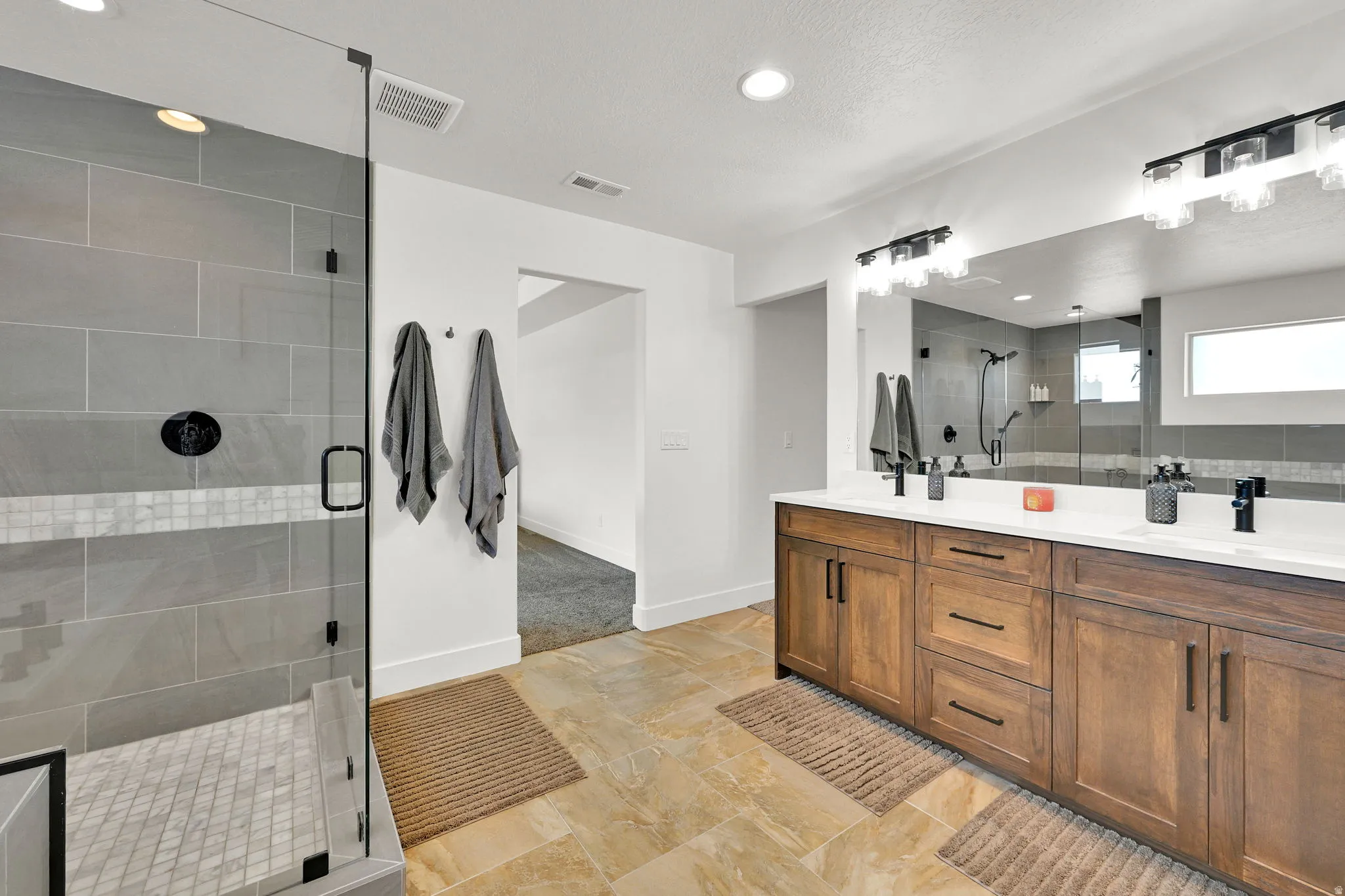 Spacious bathroom featuring a dual vanity with wood-finish cabinetry, white countertops, and matte black fixtures