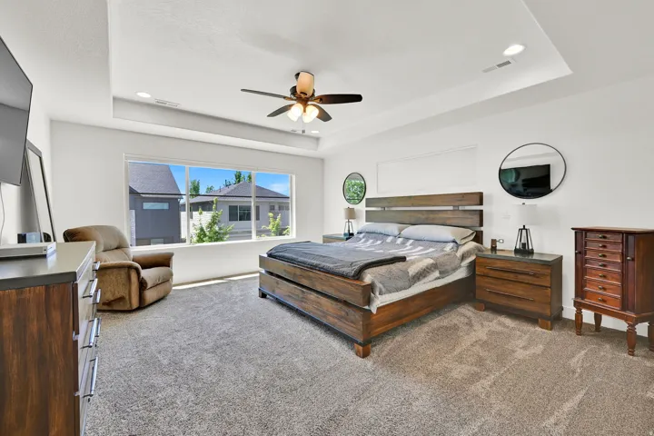 Spacious bedroom with a tray ceiling and recessed lighting, featuring a wide window, ceiling fan, and carpeted flooring