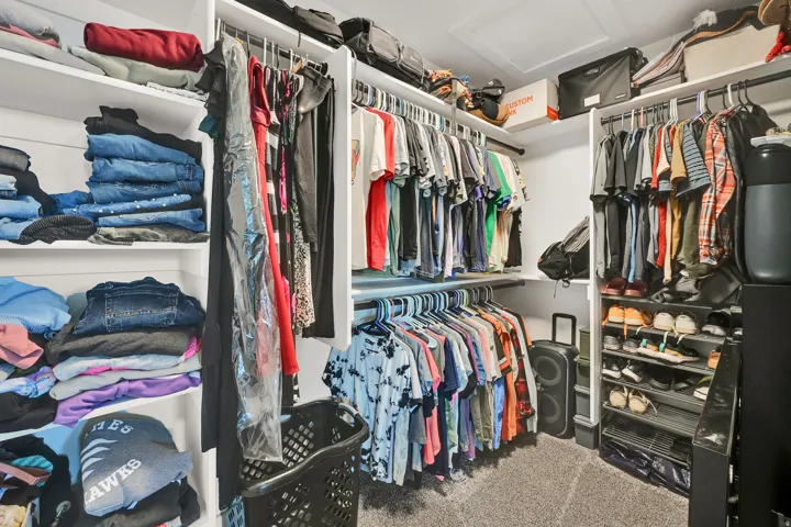 Walk-in closet featuring built-in shelving, multiple hanging rods, carpet flooring, and a ceiling access panel