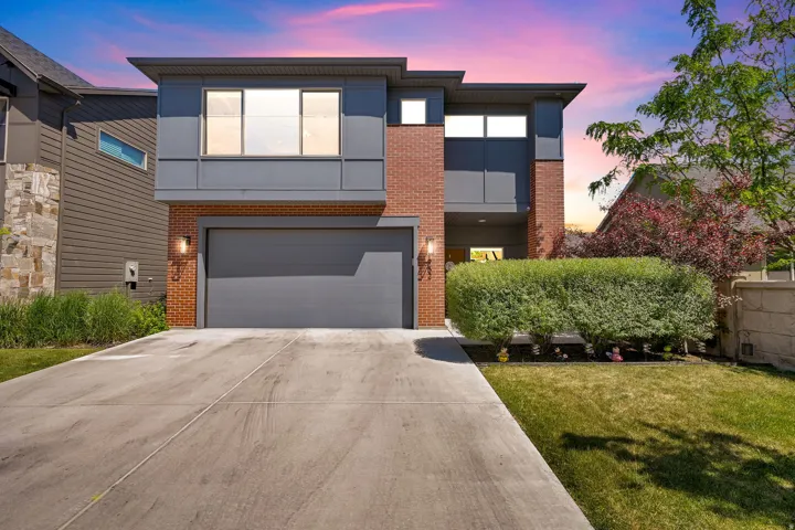 Contemporary exterior featuring brick and gray paneling, an attached garage, a concrete driveway, a manicured lawn, and mature landscaping