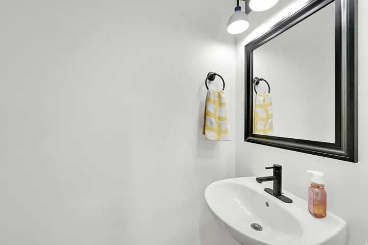 White wall-mounted sink with a matte black faucet, framed mirror, and overhead lighting fixture