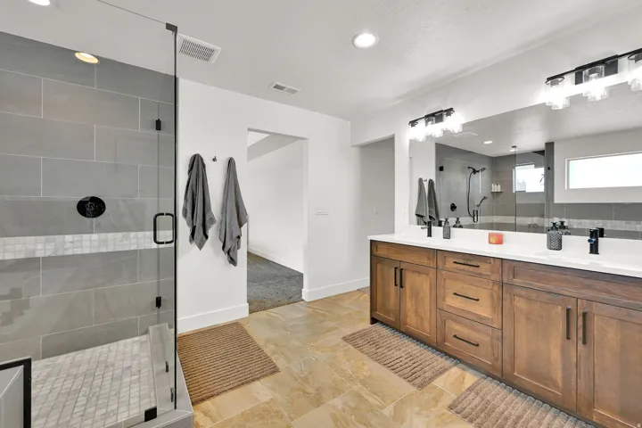 Spacious bathroom featuring a dual vanity with wood-finish cabinetry, white countertops, and matte black fixtures