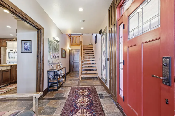 Entryway featuring a red wood door with leaded glass panels, slate-finish tile flooring, recessed lighting, wood-trimmed doorways, and a wooden staircase