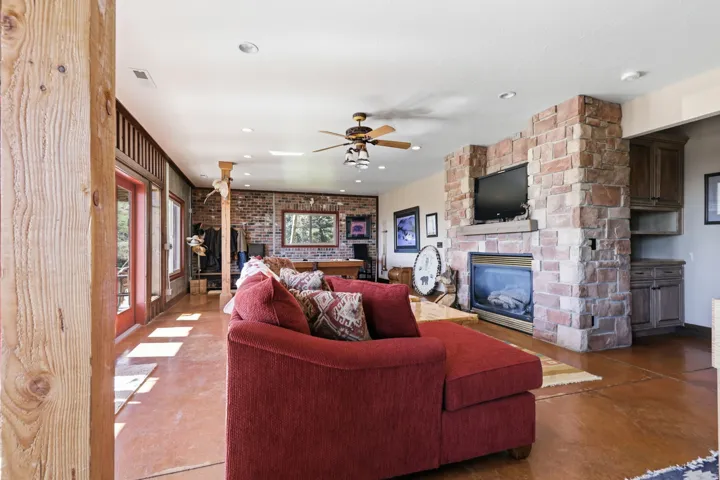 Spacious room featuring a stone fireplace with a built-in hearth, stained concrete flooring, a ceiling fan, and multiple French doors