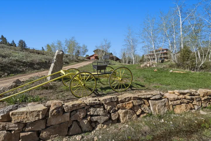Stone retaining wall with a decorative yellow wagon, a winding dirt road, and mature trees