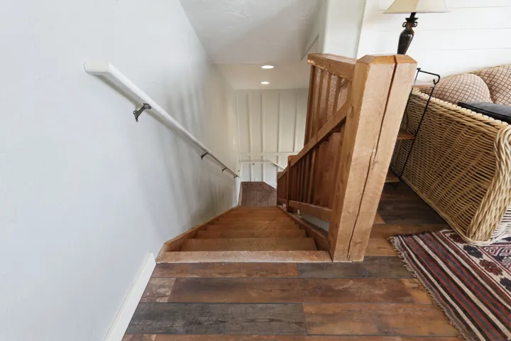 Staircase featuring wood-finish flooring and steps, natural wood handrail and balusters, a white wall-mounted handrail, and recessed lighting