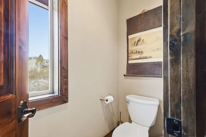 Powder room with a white toilet, neutral wall paint, and a wood-framed window offering an outdoor landscape