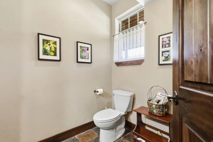 Powder room with a white toilet, slate tile flooring, and a window with wood trim