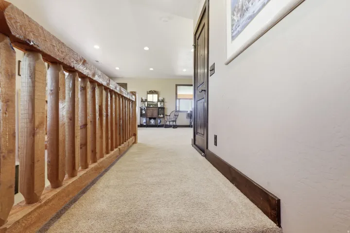 Carpeted hallway featuring a natural wood railing, recessed ceiling lights, and a dark wood paneled door