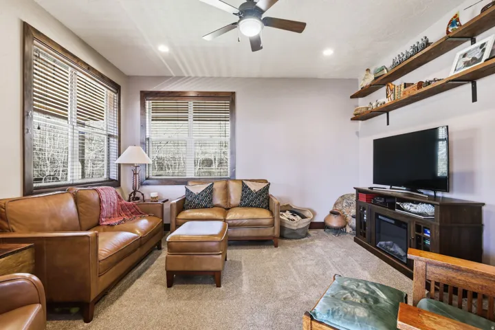 Carpeted living space featuring recessed lighting, a ceiling fan, and two large windows with horizontal blinds and wood trim