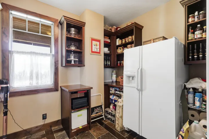 Kitchen pantry featuring extensive built-in dark wood cabinetry, a window with wood-frame trim, and slate-style floor tiling
