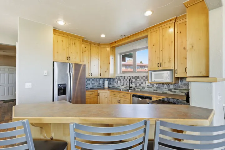 Kitchen featuring warm-toned wood cabinetry, stainless steel appliances, a patterned tile backsplash, and a breakfast bar with an overhang