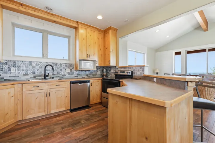 Kitchen featuring wood-finish cabinetry, stainless steel appliances, a patterned tile backsplash, and wood-finish flooring