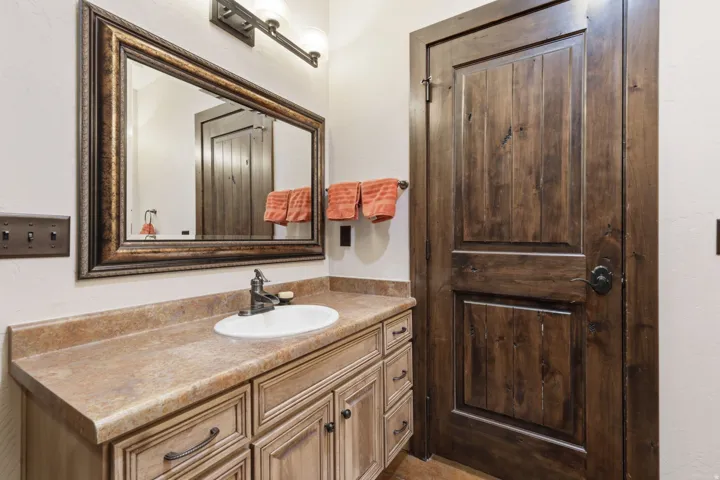 Bathroom vanity featuring a light wood-finish cabinet with dark hardware, a tan stone-look countertop, and an undermount sink with a bronze-tone faucet