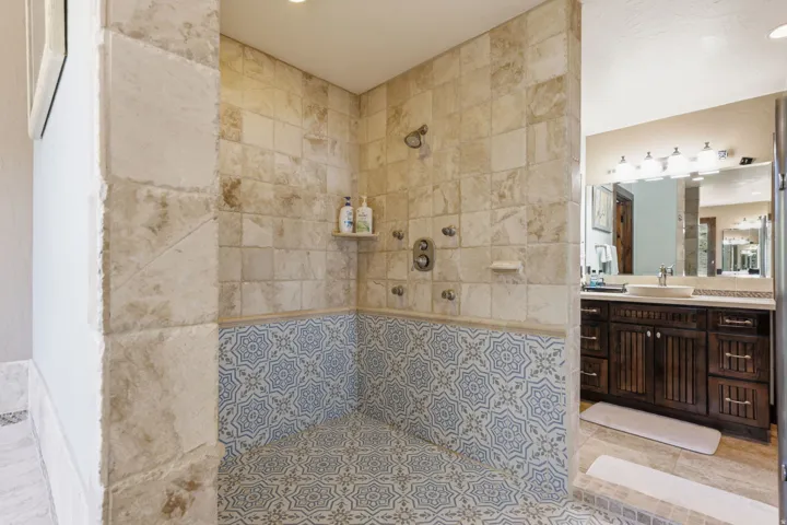 Walk-in shower with full-height stone-look tile walls, a patterned blue and white tile wainscoting, and a coordinating tile floor