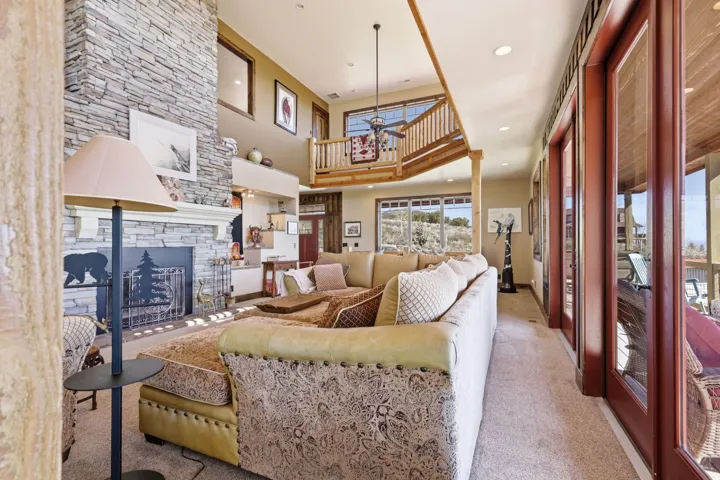 Great room featuring a floor-to-ceiling stacked stone fireplace, a wood-finish vaulted ceiling, and multiple glass doors opening to the exterior