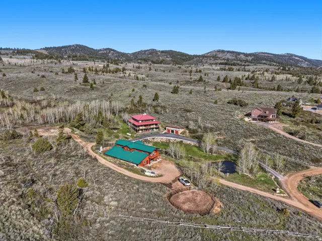 Expansive property featuring three distinct structures with vibrant roofing, set against a backdrop of rolling hills