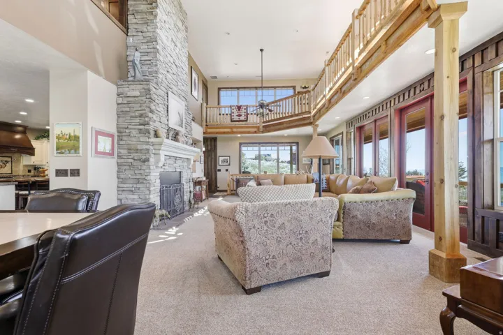 Spacious interior featuring a stone-clad fireplace with mantel, exposed wood beams, and a second-story wooden railing