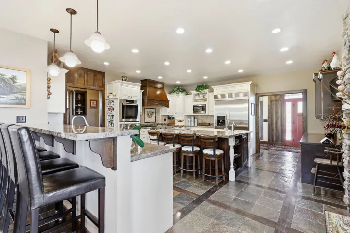 Spacious kitchen featuring an expansive island with a stone-finish countertop, ample seating, integrated stainless steel appliances, and a wood-finish range hood
