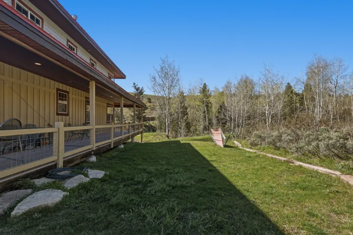 Spacious side yard featuring a wrap-around porch with wire mesh railing, board and batten siding, multiple windows, and a metal roof