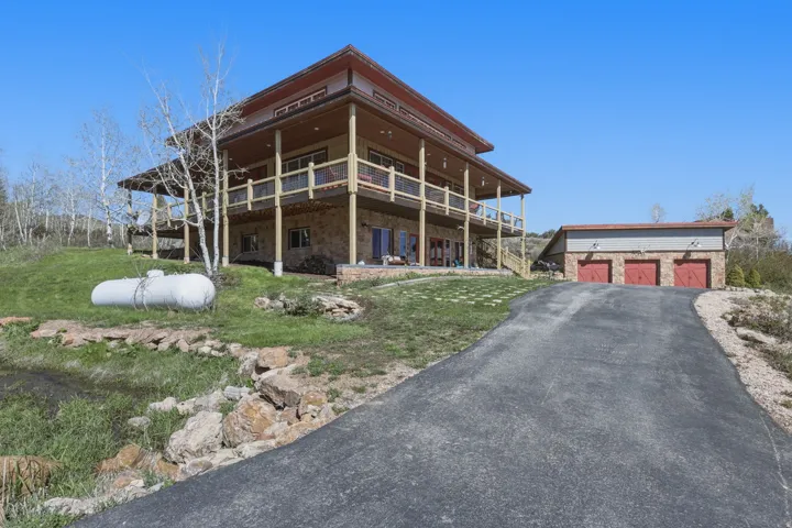 Multi-level home featuring extensive wrap-around decking, stone veneer lower level, and a detached three-car garage with red doors