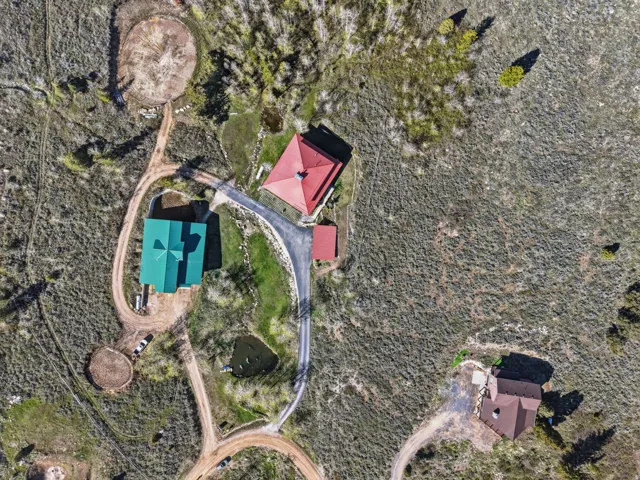 Expansive property featuring three distinct structures with varying roof colors, meandering dirt roads, and a natural pond