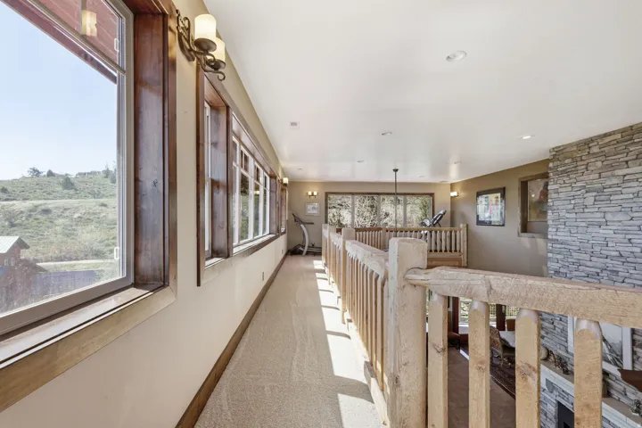 Expansive upper-level hallway with a stone-accented wall, natural wood railings, and multiple windows