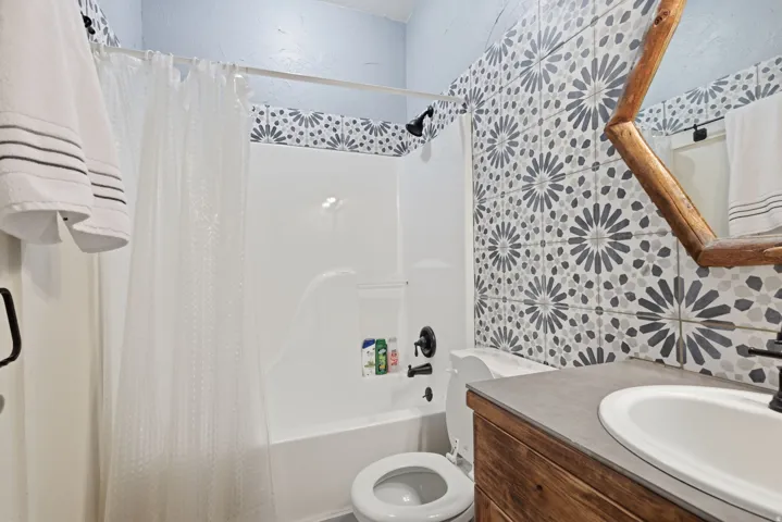 Bathroom featuring a white tub with dark bronze fixtures, patterned tile wall, wood-finish vanity with an integrated sink, and light blue wall paint