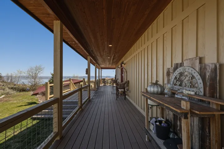 Covered wooden deck with composite flooring, wood-paneled ceiling, board and batten siding, and metal wire railing