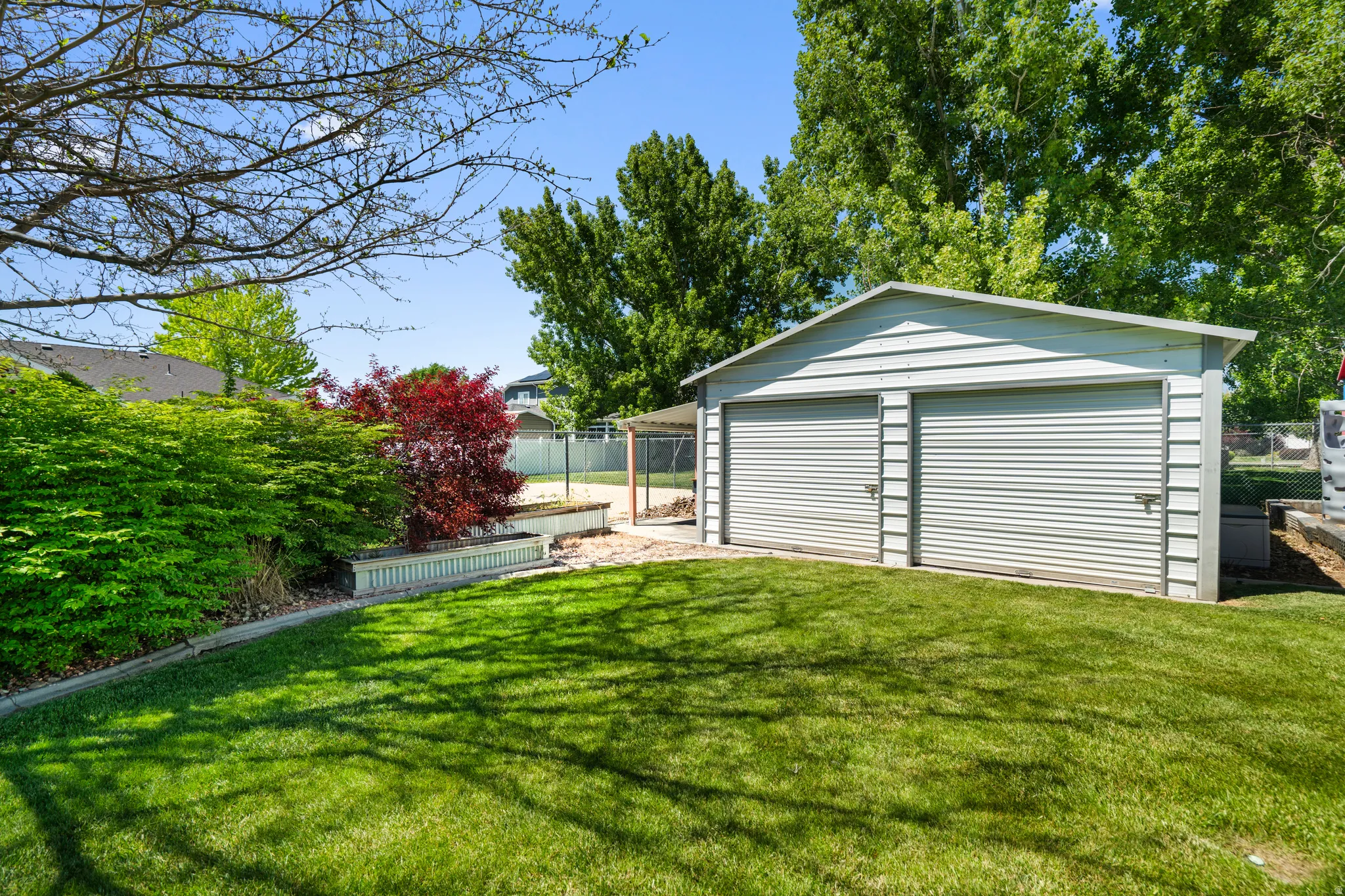 Expansive green lawn with a two-car shop featuring roll-up doors, surrounded by mature trees and shrubs