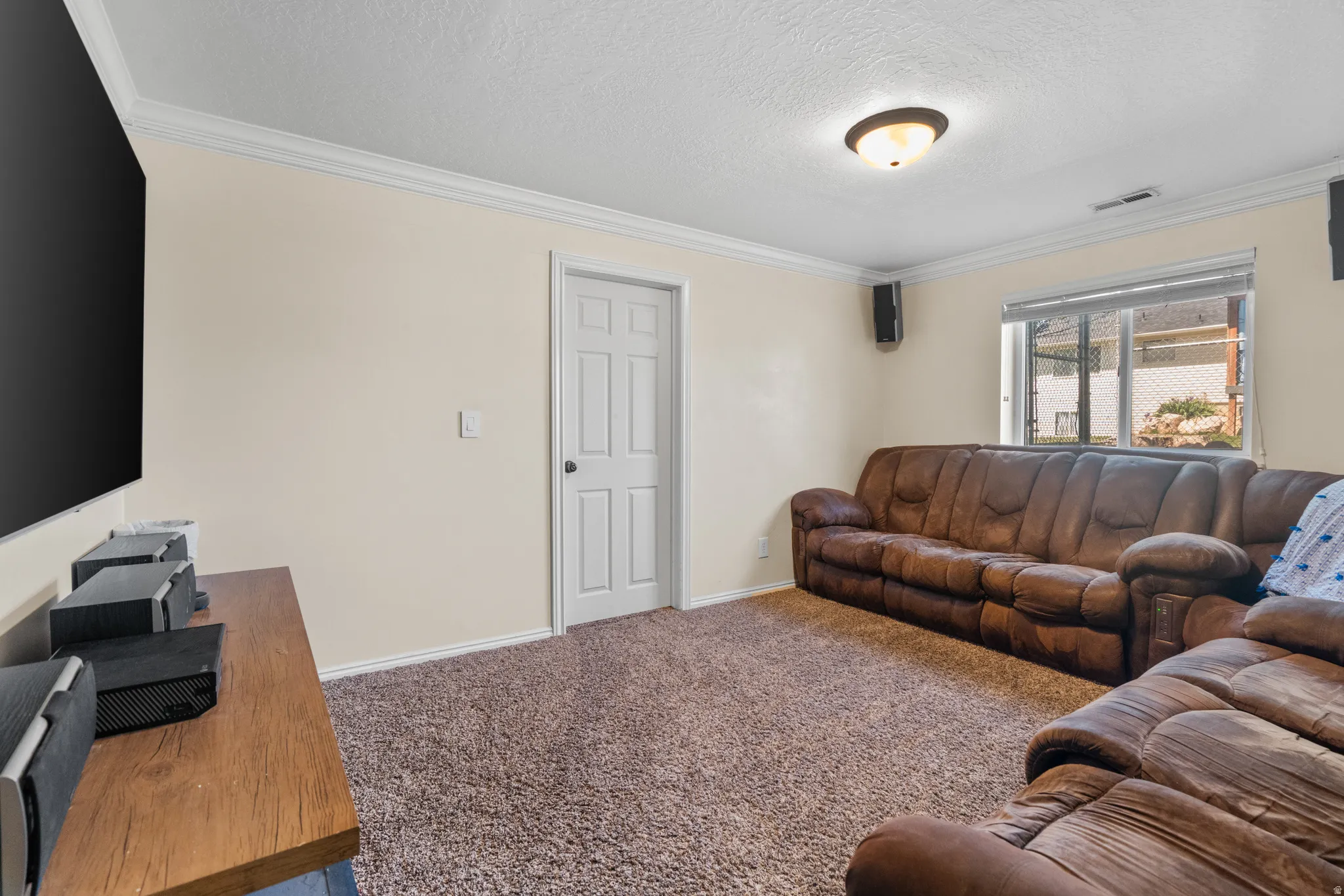 Spacious room featuring neutral painted walls, crown molding, a patterned carpet, and a window with horizontal blinds
