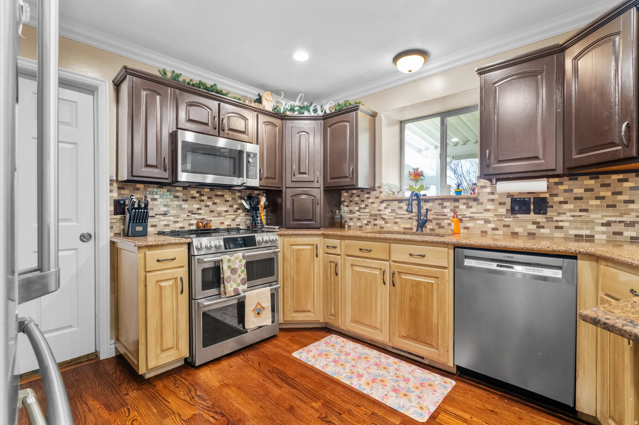 Kitchen featuring hardwood flooring, two-tone cabinetry, stainless steel appliances, a mosaic tile backsplash, and granite countertops