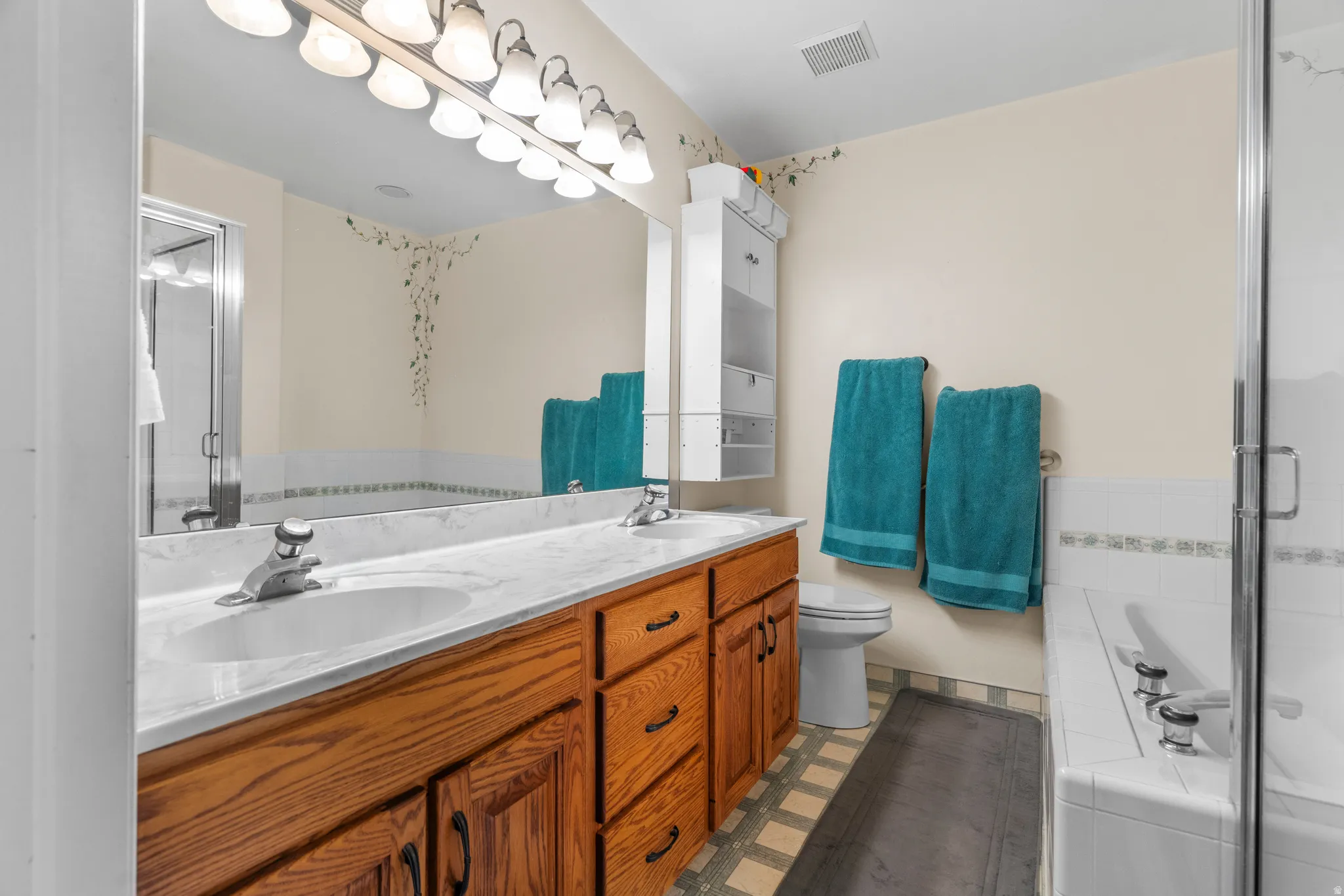Master ensuite bathroom featuring a double vanity with wood cabinetry and a light-toned countertop, dual sinks, bath and shower