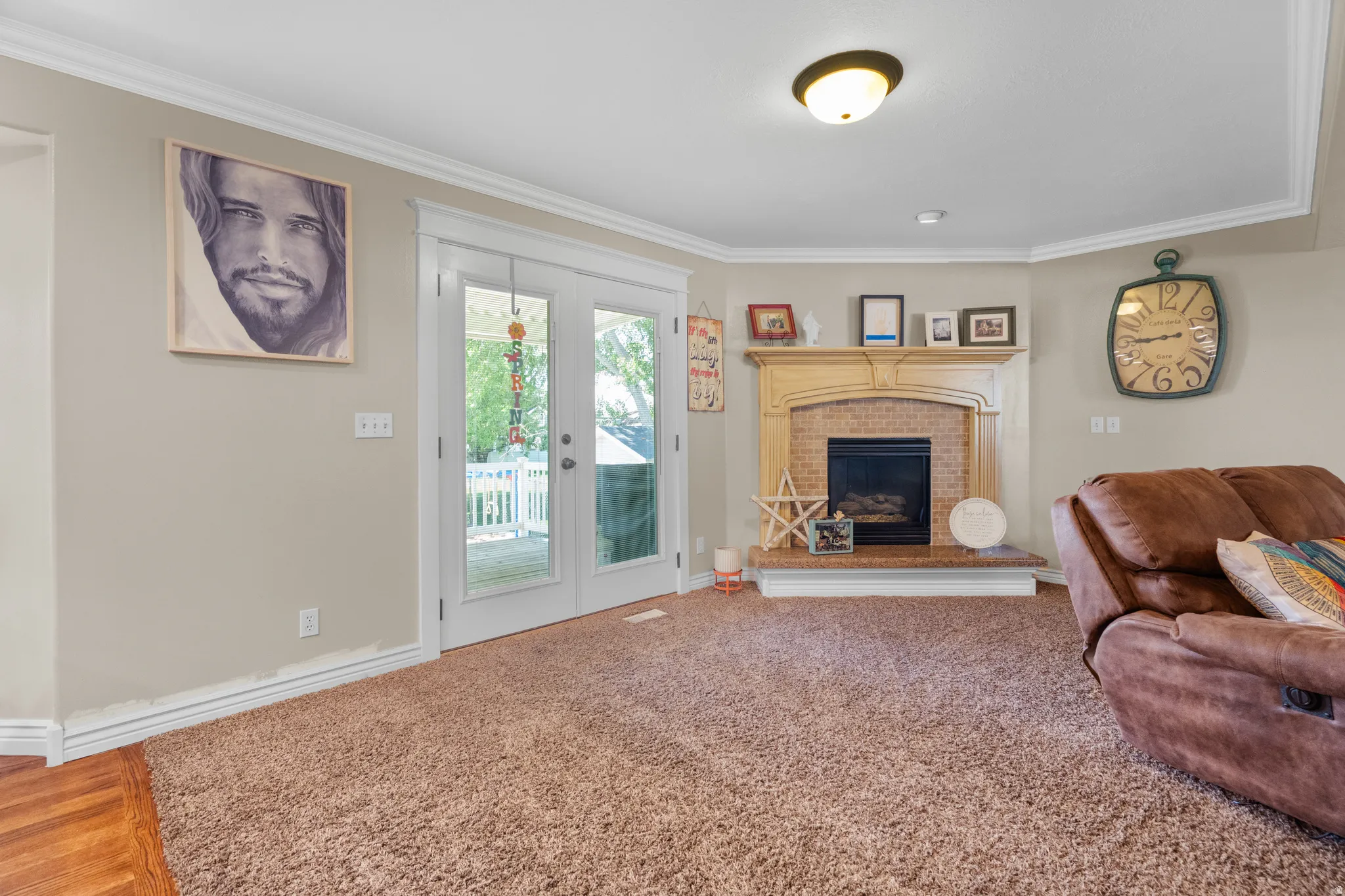 Living space featuring a corner fireplace with a brick surround and wood mantel, white crown molding, and double glass-paneled doors opening to an outdoor area
