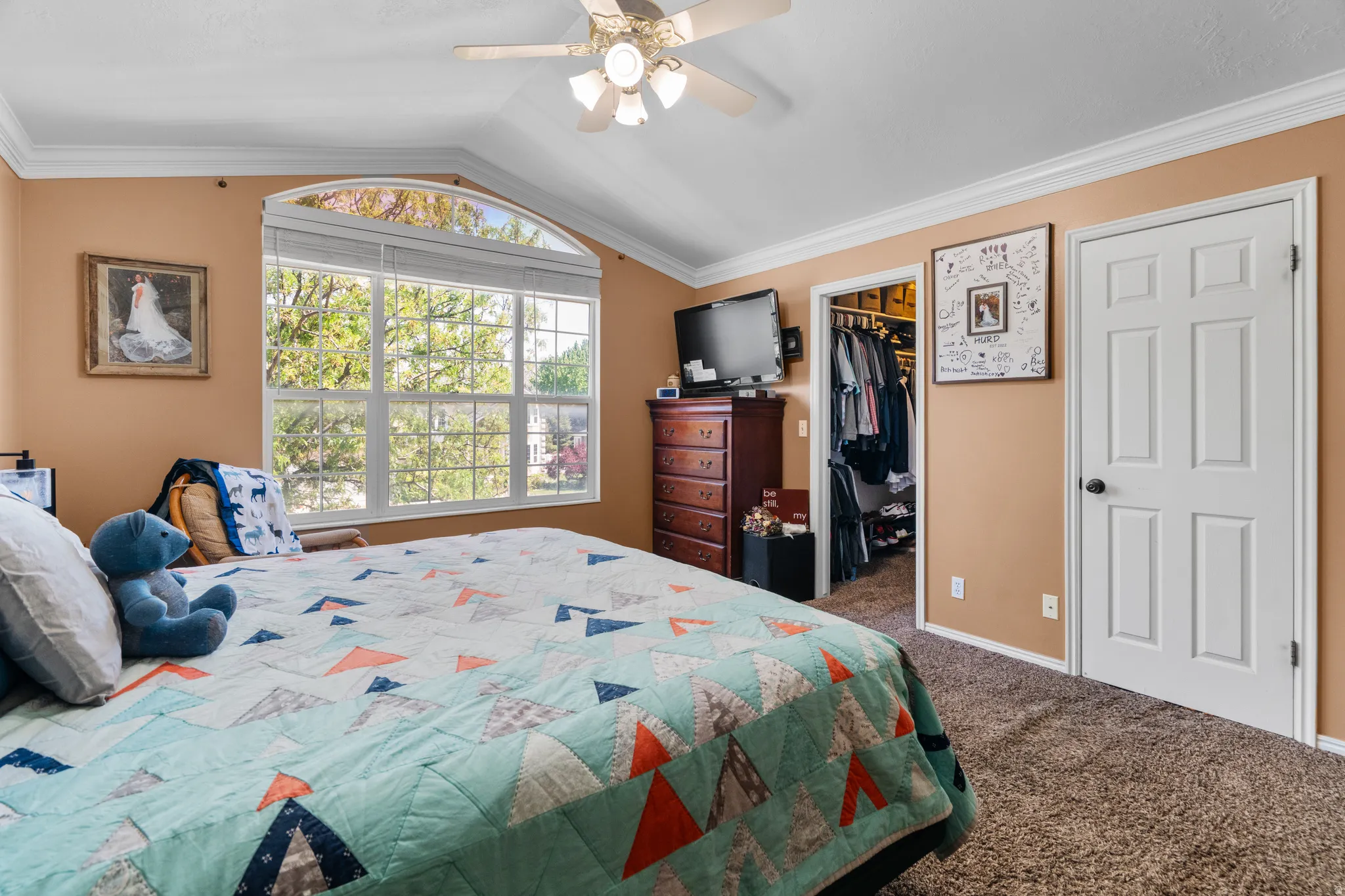 Master bedroom featuring a large arched window, vaulted ceiling, and crown molding