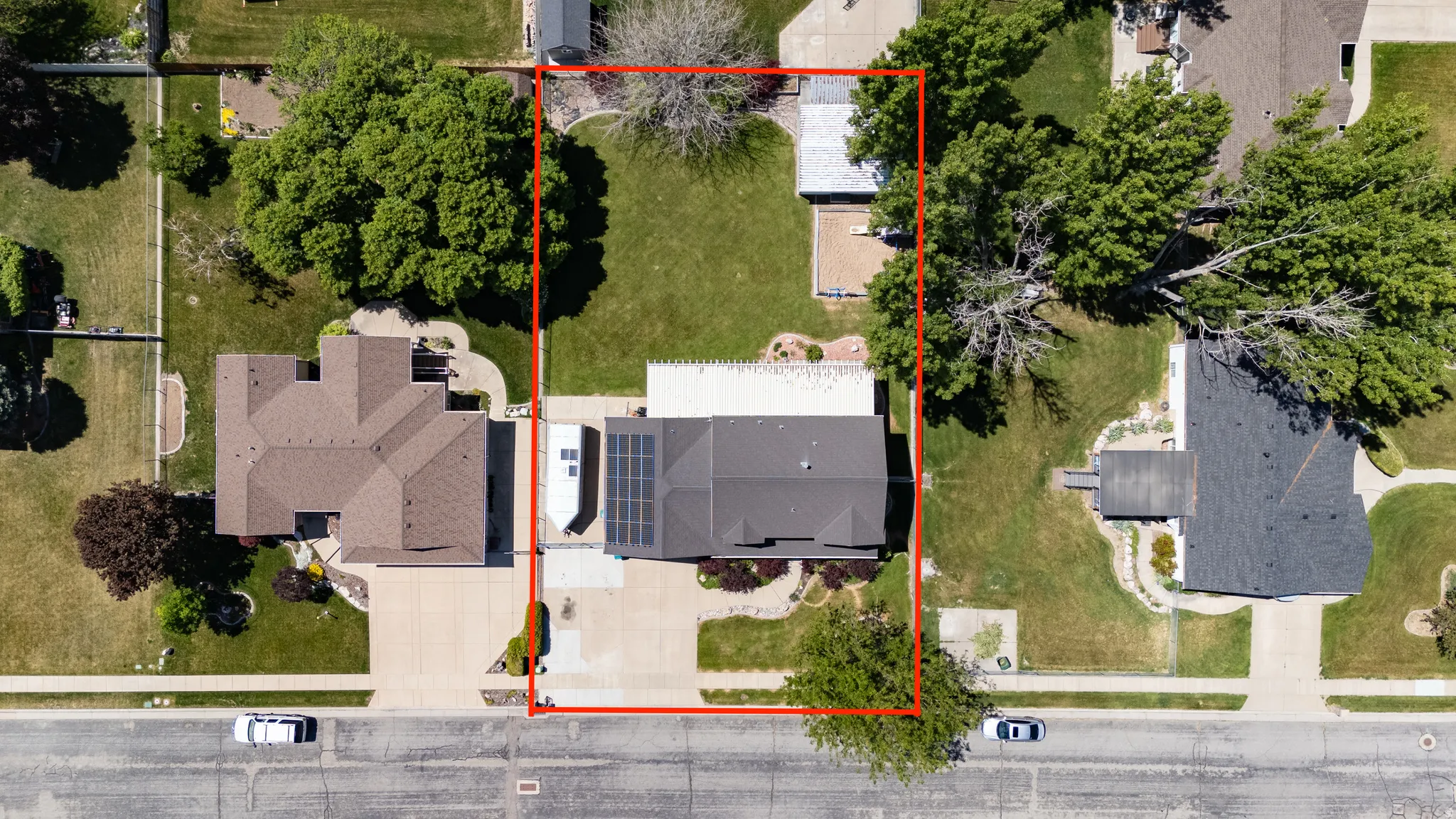 Aerial property view featuring a dark shingle roof, a paved driveway, and established landscaping