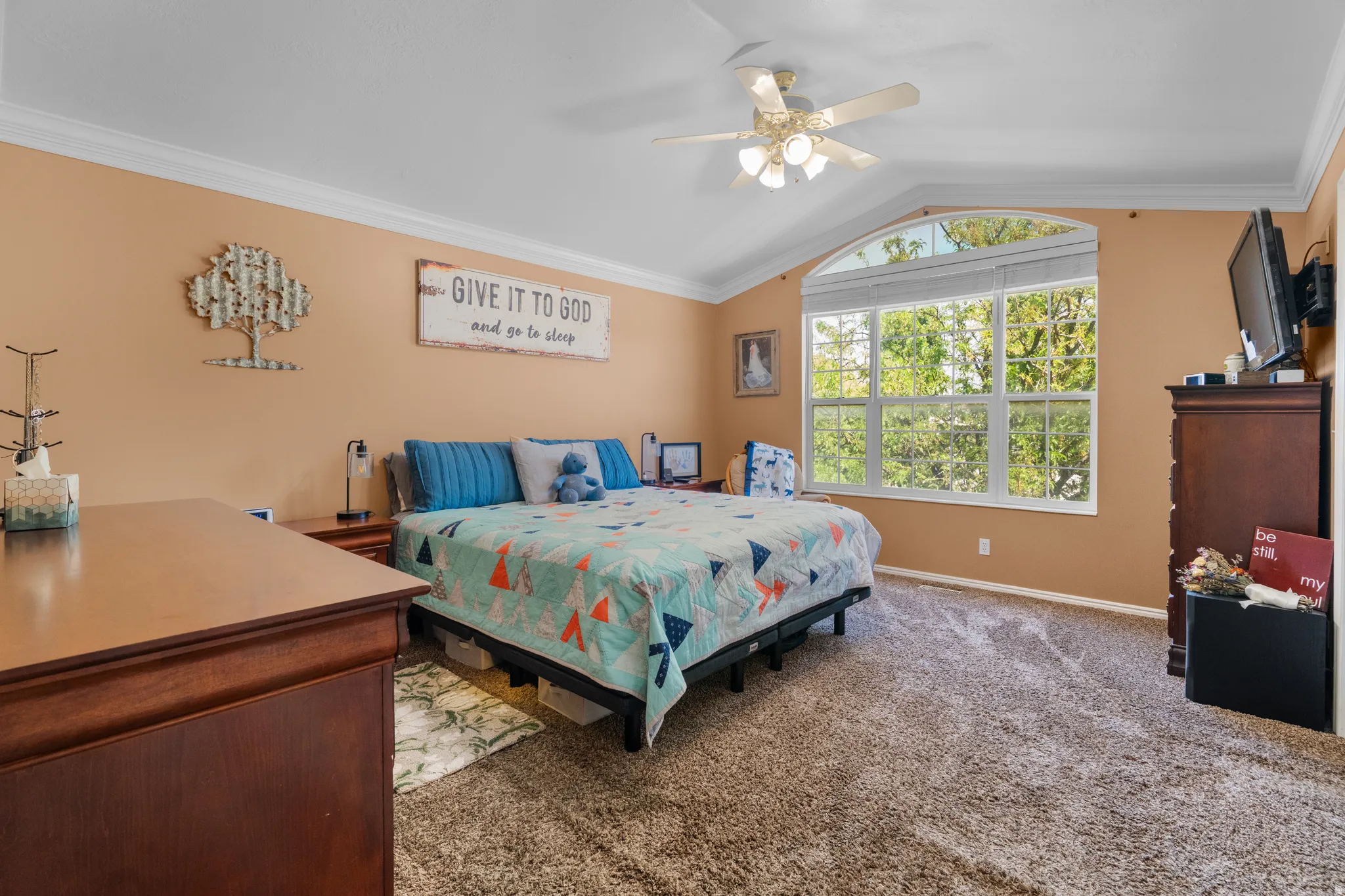 Master bedroom featuring vaulted ceilings, crown molding, a multi-pane arched window, and plush carpet flooring