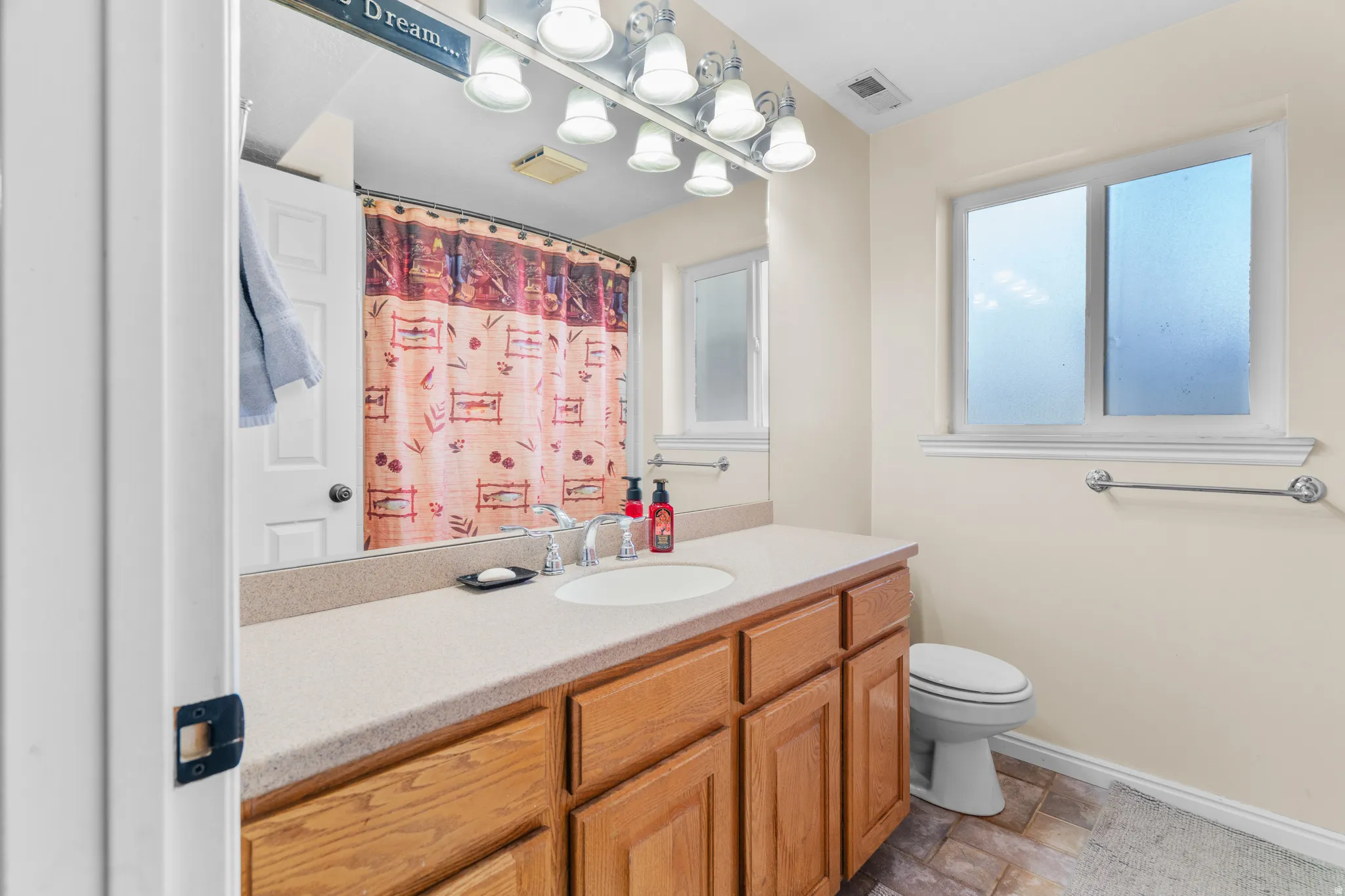 Full guest bathroom featuring a light-toned countertop, wood-finish cabinetry, an integrated sink with chrome faucet, and a toilet